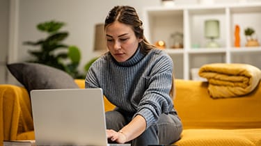 Young,Woman,Working,From,Home,,Using,Her,Laptop,On,A